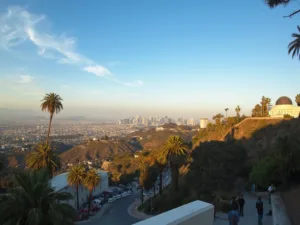 "Griffith Observatory in the foreground during golden hour in November, with views of palm trees, the Hollywood sign, and downtown LA skyscrapers, tourists on the viewing deck, and LA's typical fall golden-orange light"