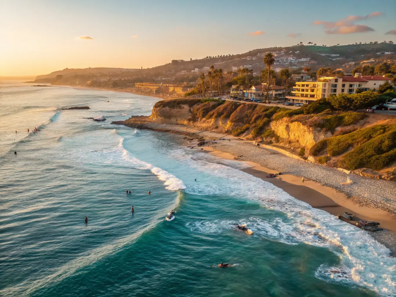 Panoramic view of La Jolla coastline featuring crystal clear waters, golden sand beaches, surfers riding waves, and warm September sunlight illuminating the landscape