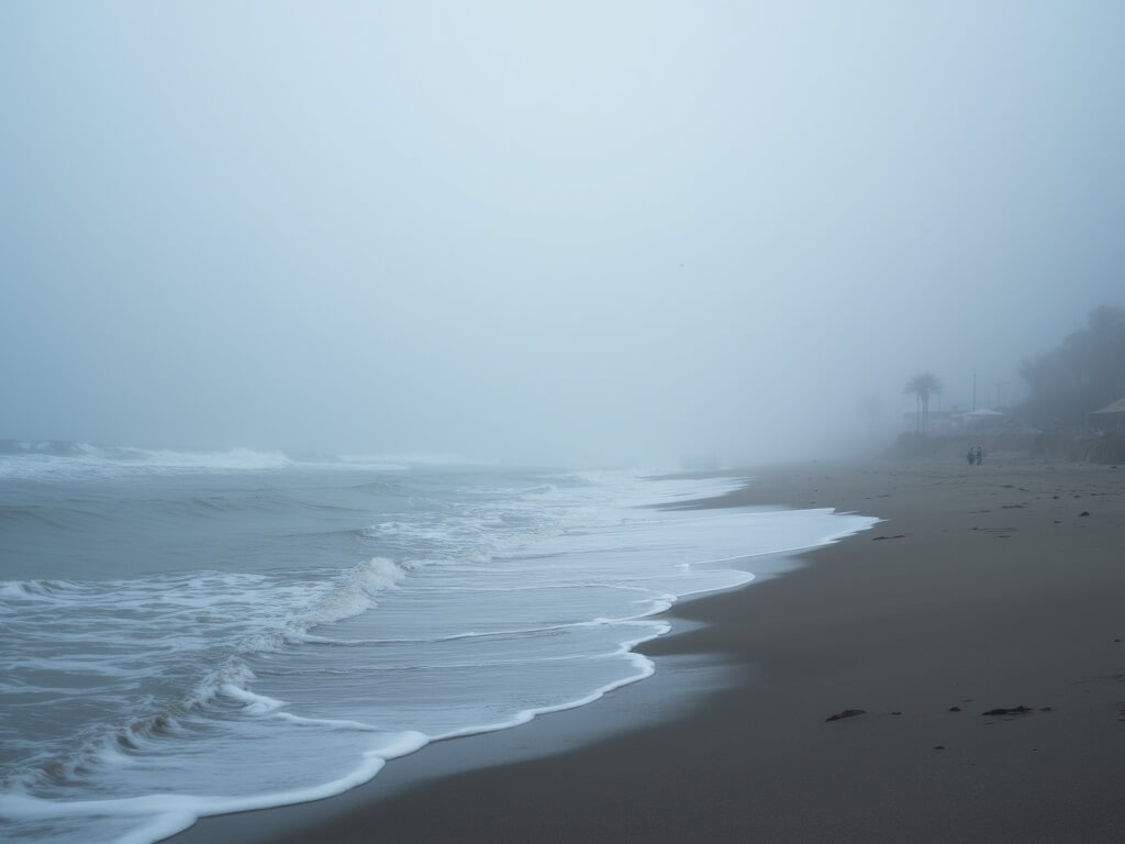 Misty dawn at Huntington Beach with low-lying fog, barely visible silver-gray waves, and soft morning light creating a serene atmosphere.