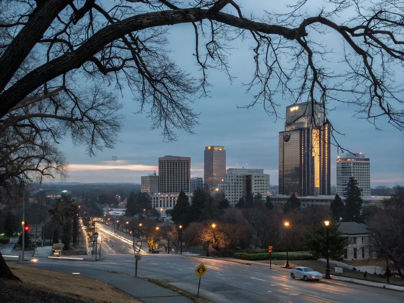 Winter dusk in Sacramento with soft light casting long shadows across urban streets and bare tree branches silhouetted against a cool blue and gray sky