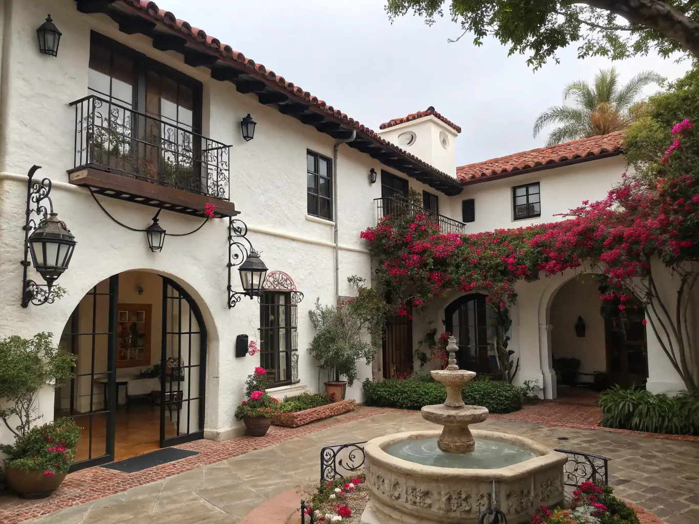 Spanish Colonial style boutique hotel in Santa Barbara with white stucco walls, red tile roof, and wrought iron details, featuring a peaceful courtyard with a fountain and blooming bougainvillea.