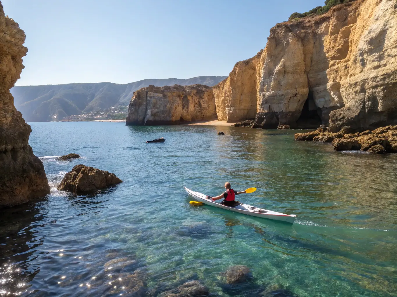 Single kayaker exploring crystal-clear waters near Santa Barbara's coastline, with sunlight shimmering on the water and rugged cliffs in the background