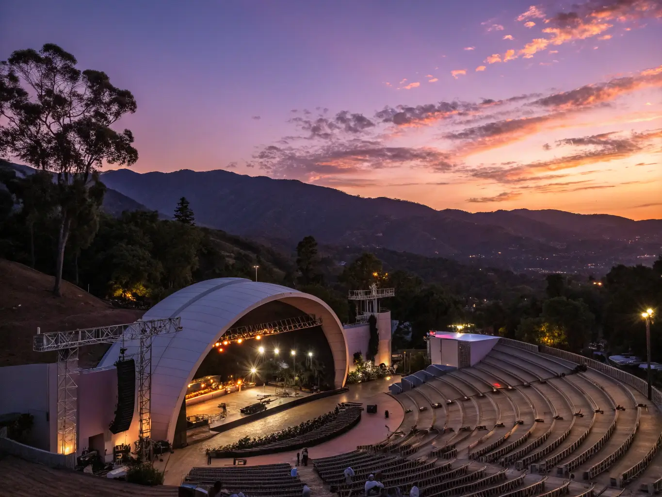 Twilight shot of Santa Barbara Bowl amphitheater with illuminated stage lights against a purple-orange sunset sky, mountains in the background