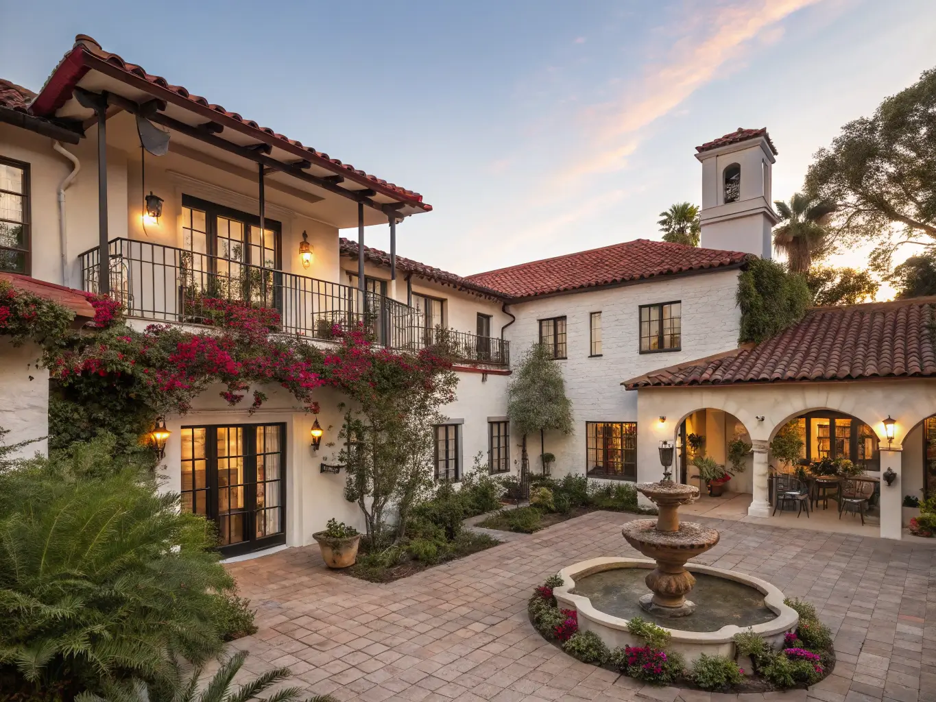 Spanish Colonial-style boutique hotel at golden hour with stucco walls, terracotta roof, wrought iron balconies with bougainvillea, and a central courtyard with a fountain and Mediterranean plants