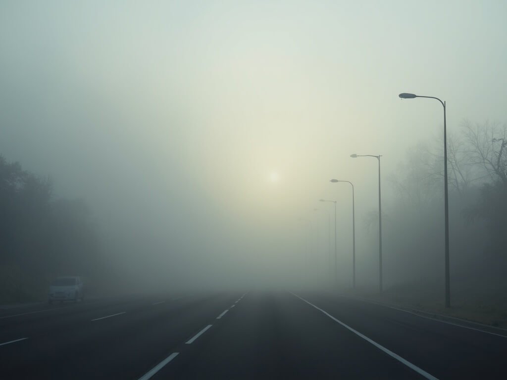 Bakersfield in December: A Hidden Winter Wonderland You Never Knew Existed Dense winter fog shrouding a Bakersfield highway with barely visible street lamp silhouettes, muted grays and whites, in early morning light