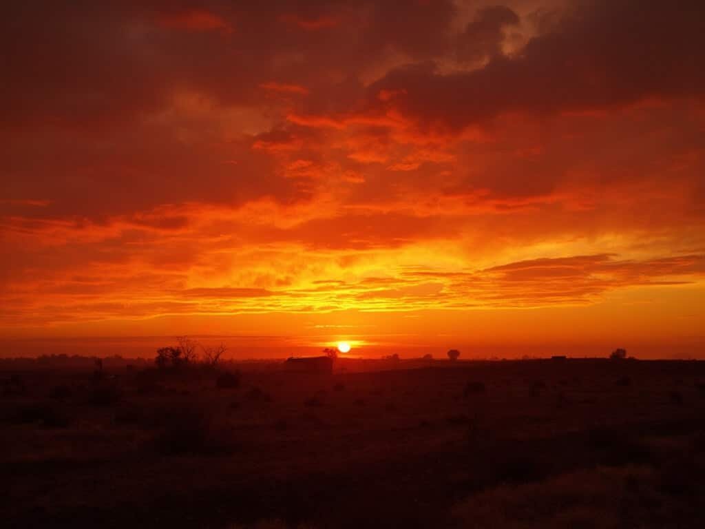 Dramatic sunset in Fresno with orange and crimson sky, silhouetting dry agricultural fields and distant heat haze