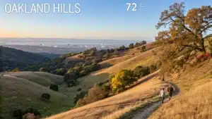 "Panoramic view of Oakland Hills during October's golden hour featuring hikers, autumn-touched California oaks, the distant San Francisco Bay, clear city skyline, and warm autumn tones, at 72°F"