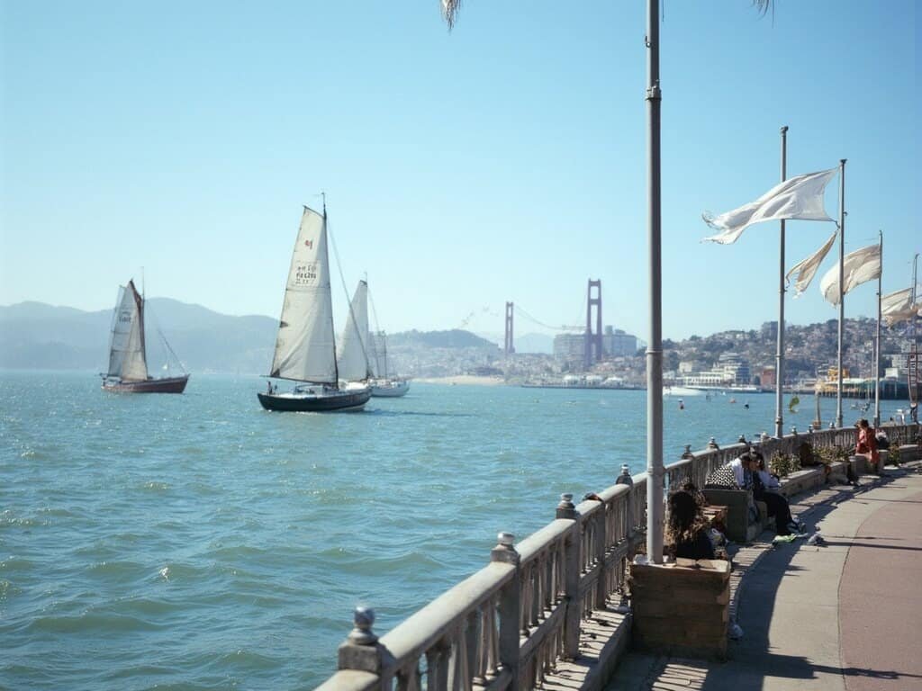 Sailboats gliding across San Francisco Bay at Jack London Square, illustrating the city's natural air conditioning effect through water ripples and waving flags