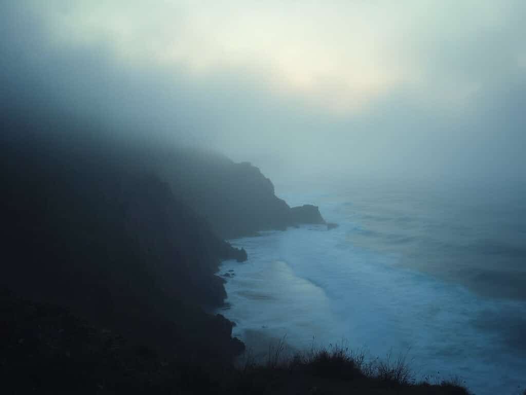 Marine fog engulfing Monterey's rocky coastline at dawn, creating a ethereal atmosphere
