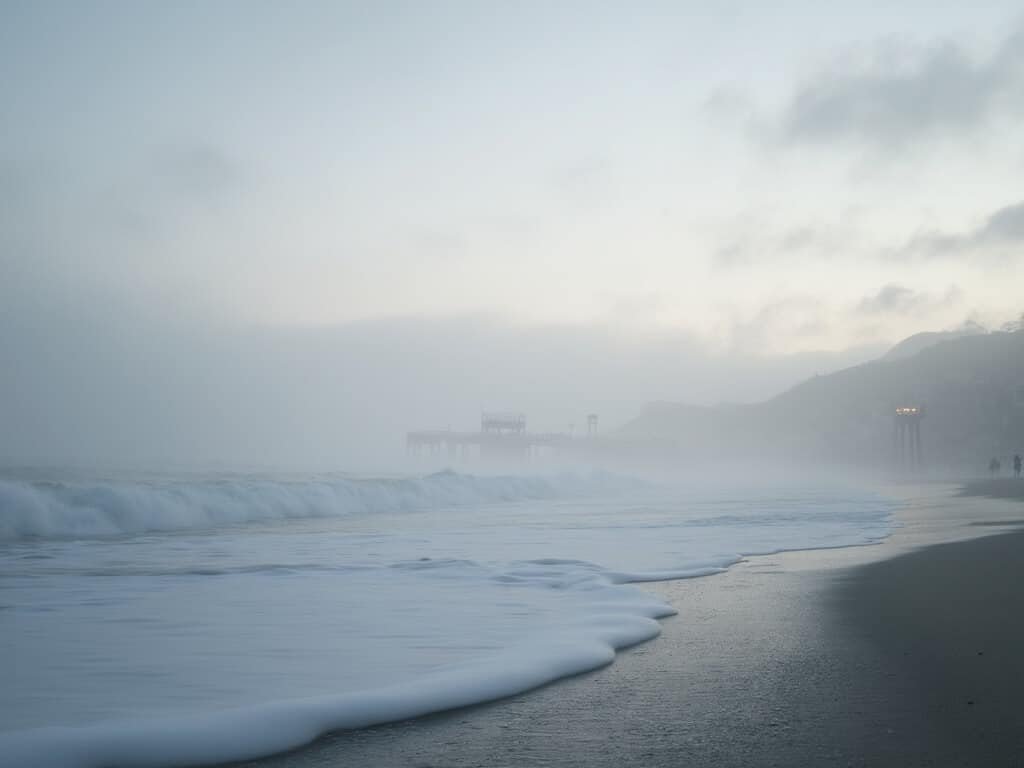 Misty dawn at Pismo Beach with pier silhouettes and calm ocean waves