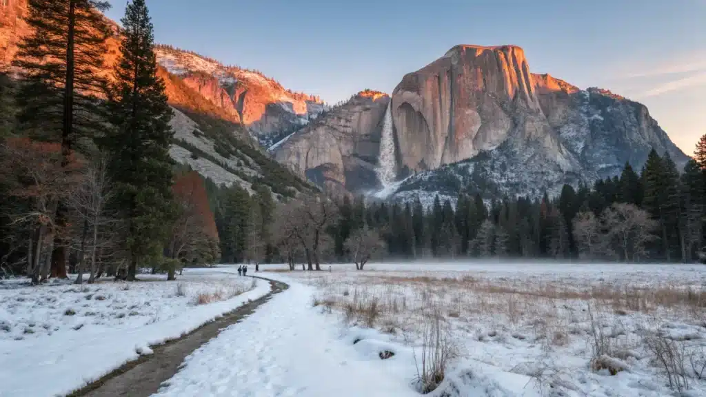 Why Yosemite Village in December Is Nothing Like You'd Expect (And That's a Good Thing) "Winter sunrise over Cook's Meadow in Yosemite Valley with snow-covered Yosemite Falls and Half Dome, a few tiny figures on the trail emphasizing solitude"