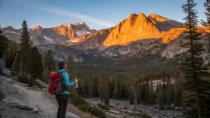 Person on a mountain trail at Mammoth Lakes during a golden sunrise, wearing layered clothing and applying sunscreen, with Sierra Nevada peaks, pine trees, and a thermometer showing 48°F in the background.