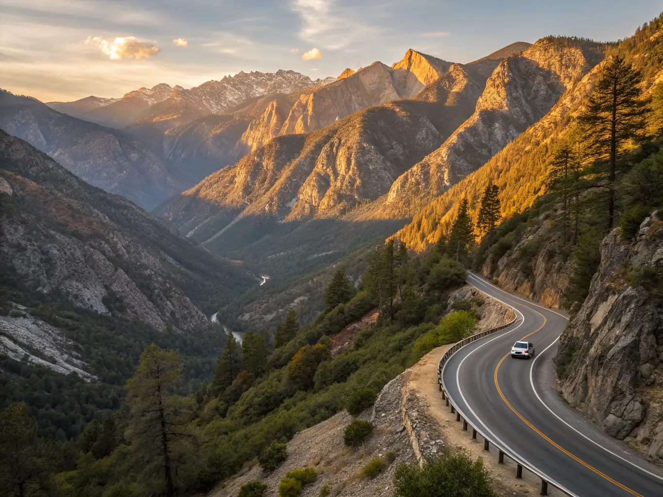 The Best California Road Trips, From Someone Who's Driven Most of Them Aerial view of Highway 180 winding through Kings Canyon toward Cedar Grove, with golden-lit granite cliffs, deep shadowed canyon, snow-capped peaks, and a lone car highlighting the vast landscape.