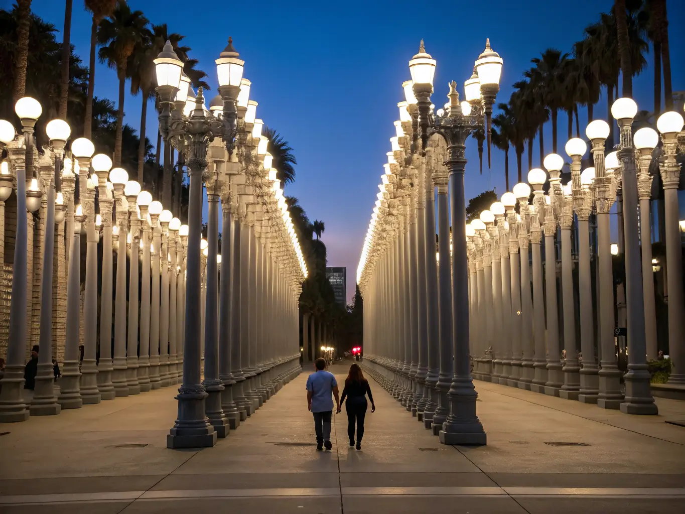 Free Things to Do in Los Angeles If You'd Rather Not Spend a Fortune A nighttime photo of LACMA’s Urban Light installation, glowing vintage street lamps lining a walkway where a couple strolls hand in hand under a deep blue sky.