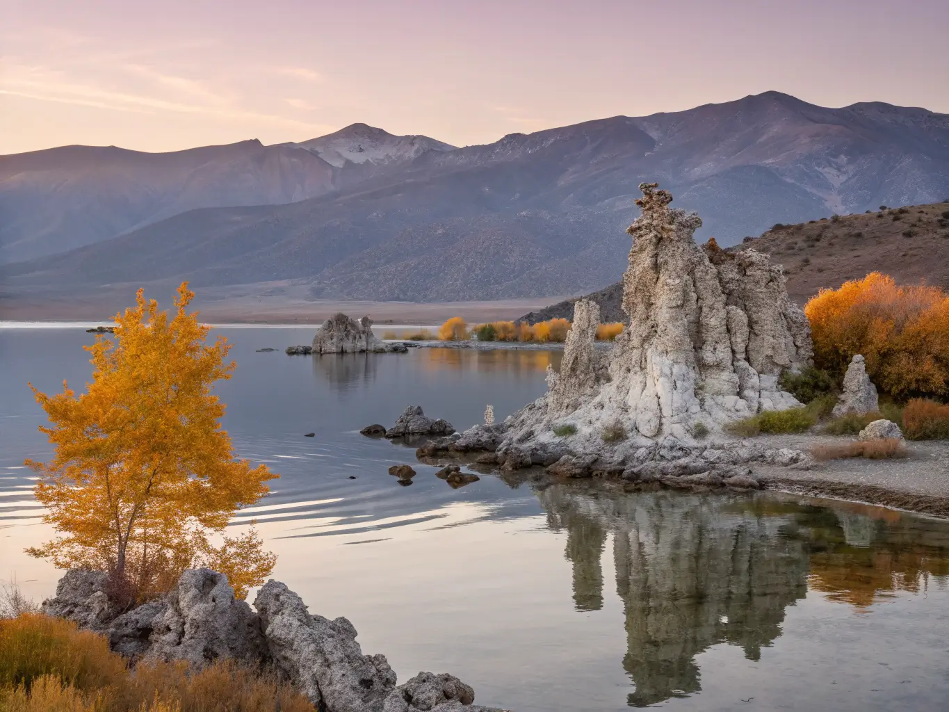The Best California Road Trips, From Someone Who's Driven Most of Them Autumn morning at Mono Lake with pale tufa towers reflected in calm water, soft amber light, gentle mist, and distant golden aspens beneath pastel sky.
