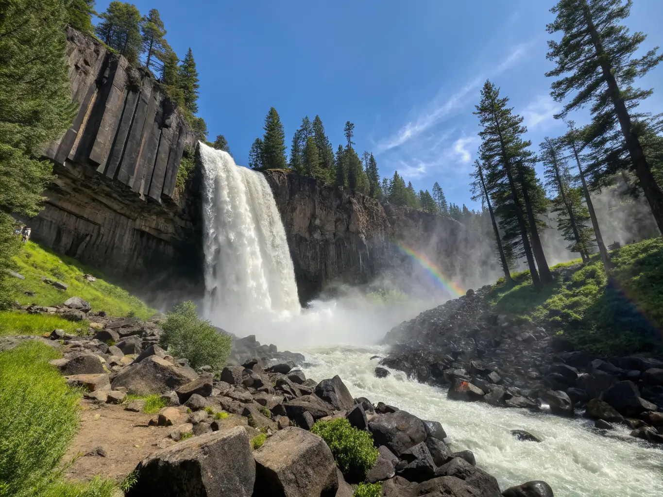 June Might Be the Best Month to Visit Mammoth Lakes Wide-angle view of Rainbow Falls near Devils Postpile, powerful snowmelt waterfall framed by dark basalt columns, morning mist forming a faint rainbow under a bright blue Sierra sky.