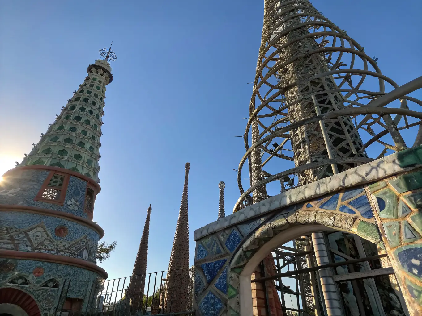 Free Things to Do in Los Angeles If You'd Rather Not Spend a Fortune Low-angle view of the Watts Towers in Los Angeles, sunlight highlighting the intricate mosaic of steel, pottery, and glass spires against a clear blue sky.